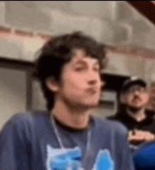 a man in a blue shirt is making a funny face while standing in a crowd .