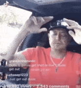 a man in a red shirt is sitting in a car with a hat on