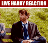 a man in a suit and tie is sitting on a bench with a sign that says live hardy reaction