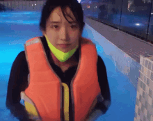 a woman wearing an orange life jacket is in a pool