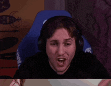 a man wearing headphones is making a funny face while sitting in a gaming chair .