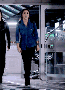 a woman in a denim shirt and black pants is walking with another woman
