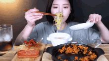 a woman is eating noodles with chopsticks and a bowl of sauce