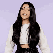 a woman with long black hair is wearing a crop top and black pants .