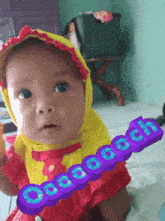a baby wearing a yellow head scarf and a red dress is holding a purple sign that says " cocoa coach "