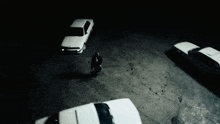 a man stands in a dark parking lot surrounded by white cars
