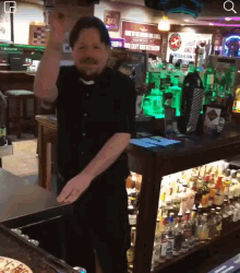 a man with a mustache is standing in front of a bar with a sign that says ' no smoking ' on the wall