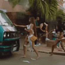 a woman in a crop top is walking down a street next to a green van