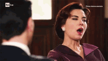 a woman in a purple dress is looking at a man in a suit and the words rai 1 hd are on the screen