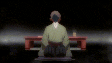 a man in a green kimono is kneeling down in front of a table in a dark room .