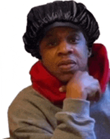 a man wearing a black hat and a red scarf is sitting with his hand on his chin .