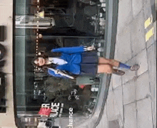 a woman in a blue jacket and skirt is standing on a sidewalk in front of a building .