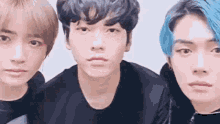 three young men are standing next to each other and looking at the camera . one of the men has blue hair .