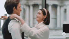 a woman adjusts a man 's tie with a white w on the bottom