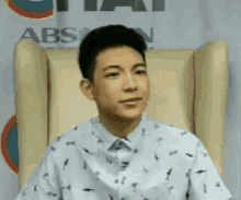 a young man is sitting in a chair wearing a white shirt and looking at the camera .