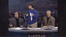 a man in a blue sweater is holding up a piece of paper in front of a wow sign
