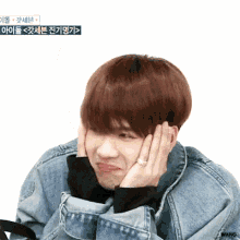 a young man in a denim jacket is making a face with his hands on his face