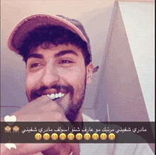 a man with a beard wearing a baseball cap is smiling with arabic writing below him