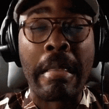a man wearing glasses and headphones looks at the camera with his eyes closed .
