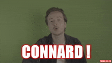 a man is standing in front of a green wall with the word connard written in red