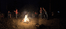 a group of people are gathered around a campfire in the woods