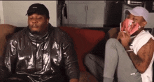 two men are sitting on a couch and one is holding a stack of money in his hand