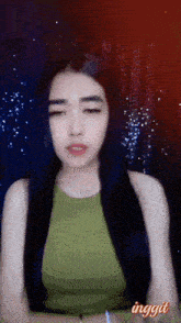 a woman with long black hair is wearing a green tank top with the word inggit on the bottom