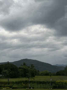 a cloudy sky over a lush green field with a mountain in the background
