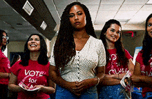 a group of women are standing in a hallway wearing red shirts that say vote for