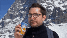 a man holds a can of sanpellegrino in front of a mountain