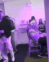 a group of people are gathered in a room with purple lights and one of them is wearing a sweatshirt that says supreme