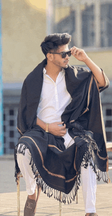 a man wearing a white shirt and a black shawl sits on a chair