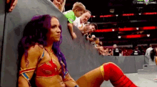 a woman in a red top and red knee pads is sitting in front of a crowd of people .