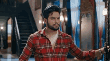 a man in a red plaid shirt is standing in a room with stairs .