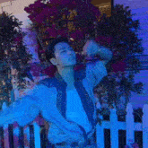 a man in a blue shirt and tie is dancing in front of a white picket fence with his arms in the air .