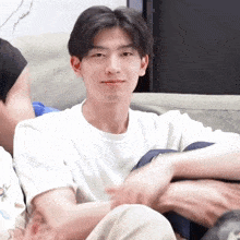 a young man in a white shirt is sitting on a couch with his legs crossed .