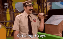 a man in a police uniform with a mustache is holding a whip and says catching strays