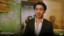 a man in a suit stands in front of a poster that says twiv