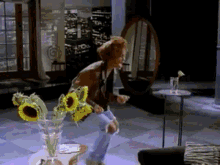 a woman is dancing in a living room with a vase of sunflowers on the table