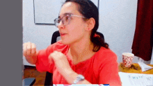 a woman wearing glasses is sitting at a desk with a cup of coffee