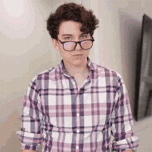 a young man wearing glasses and a plaid shirt is looking at the camera