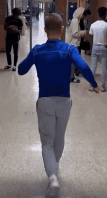 a man in a blue shirt and grey pants is walking down a hallway with other people .