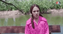 a woman in a pink shirt is sitting on a bench next to a river .