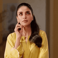 a woman in a yellow shirt has her hand to her chin