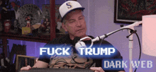 a man sitting in front of a microphone with the words " fuck trump dark web " above him