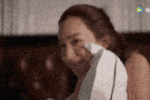 a woman wipes her face with a white towel and a play button is visible in the corner