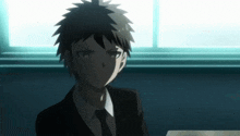 a young man in a suit and tie is sitting in front of a window