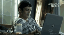 a man is sitting in front of a laptop with the words " ainda ta ai anjinho " written above him