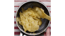 a person is stirring a sauce in a pan with a wooden spoon .