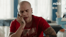 a man is talking on a cell phone while wearing a red shirt .